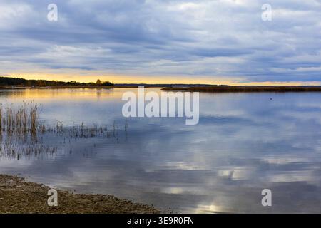 Still coastal water reflecting soft evening sky with warm light on horizon. Peaceful natural scene. Stock Photo