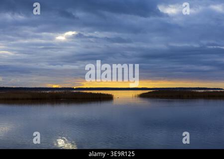 Dark clouds over calm coastal water with warm light on horizon. Atmospheric landscape. Stock Photo