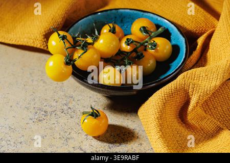 Yellow cherry tomatoes on vine in ceramic bowl with bright natural light Stock Photo