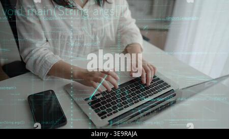 A young person works intently on a laptop, featuring programming code on the screen, representing innovation and technology in a modern workspace Stock Photo