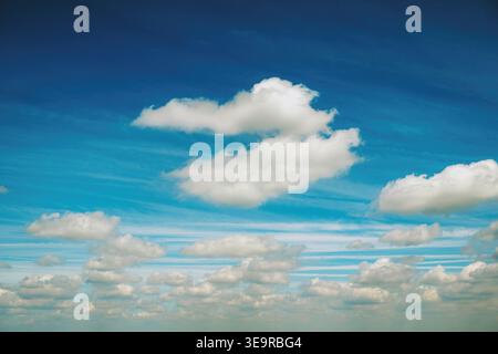 A vivid blue sky filled with layered white clouds and horizontal streaks, serene cloudscape that evokes openness, calm and atmospheric depth for backg Stock Photo