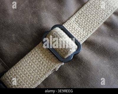 Close-up of textured beige canvas strap fastened by a utilitarian black metal buckle, resting on rugged dark brown textile—durable webbing detail for Stock Photo