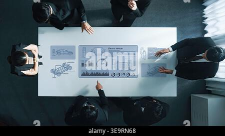 A professional business meeting centered around electric vehicle technology, showcasing a digital interface with data and visuals on a modern table Stock Photo