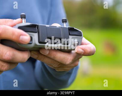 A close-up shot of two hands holding a drone remote controller with a finger about to rotate the camera tilt wheel. This action shows drone pilot skil Stock Photo