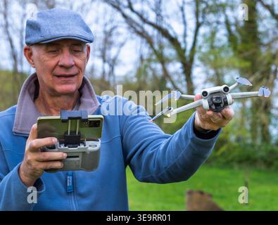 Dijon, France - April 1, 2026: A man launches a drone from his hand in a green park zone. He holds a remote controller while standing on grass. This s Stock Photo
