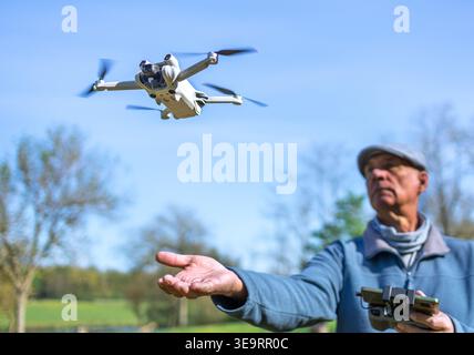 Dijon, France - April 1, 2026: A waist-up shot of a man operating a flying drone with a remote controller in a green park. This scenic nature view wit Stock Photo