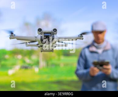 Dijon, France - April 1, 2026: A waist-up shot of a man operating a flying drone with a remote controller in a green park. This scenic nature view wit Stock Photo