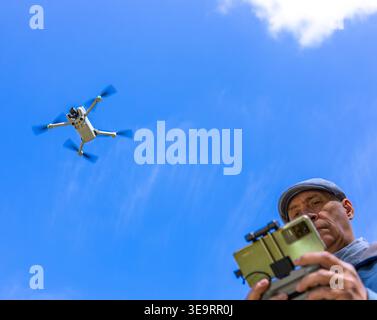 Dijon, France - April 1, 2026: A waist-up shot of a man operating a flying drone with a remote controller in a green park. This scenic nature view wit Stock Photo