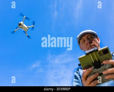 Dijon, France - April 1, 2026: A waist-up shot of a man operating a flying drone with a remote controller in a green park. This scenic nature view wit Stock Photo