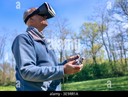 Dijon, France - April 1, 2026: A man wears virtual reality goggles to control a DJI drone in a park. This waist-up shot shows an FPV pilot using a rem Stock Photo