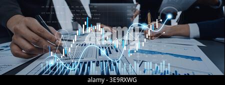 A group of business professionals work together in a modern office, analyzing financial reports and data with digital graphs appearing over the Stock Photo
