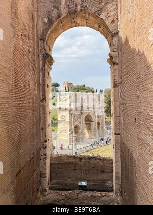 Rome, Italy - Aug 28, 2025: View through a Colosseum archway toward the Arch of Constantine, with carved reliefs and tourists in Rome, Italy. Stock Photo