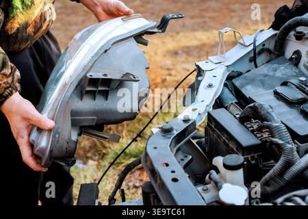 Service worker is working on their car, replacing headlight part in engine bay under service works Stock Photo
