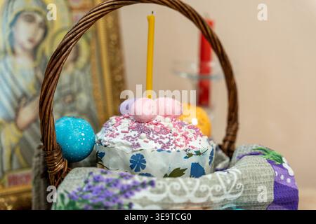 Closeup Easter Cake And Dyed Eggs Staged On Patterned Cloth, Tall Candle Rising From Basket, Delicate Sugar Sprinkles And Pastel Glaze Highlighting Stock Photo