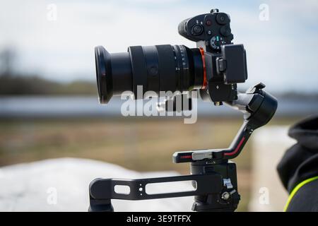 Professional mirrorless camera with large lens mounted on electronic 3-axis gimbal stabilizer for high quality video production at an industrial solar Stock Photo