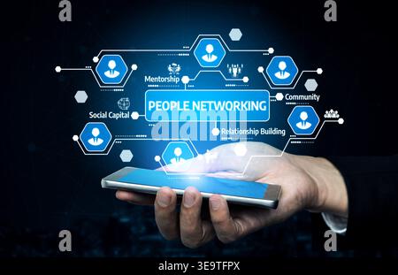 A hand holding a smartphone displays a conceptual image of people networking with digital icons, representing mentorship, community, and building Stock Photo