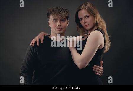 Young couple posing together, embracing against a dark background in a studio Stock Photo