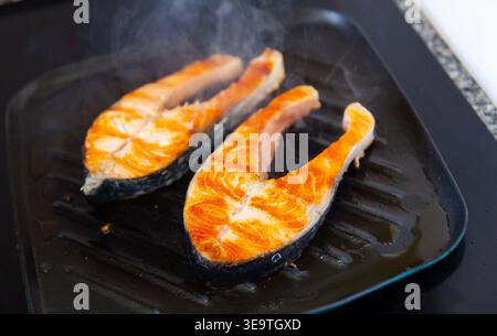 There are two pieces of broiled salmon steaks in square black frying pan Stock Photo