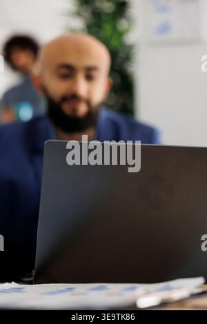 Arab company entrepreneur attending video call investor using laptop in busiess office. Executive manager discuss project strategy coworkers virtual meeting in coworking space Stock Photo
