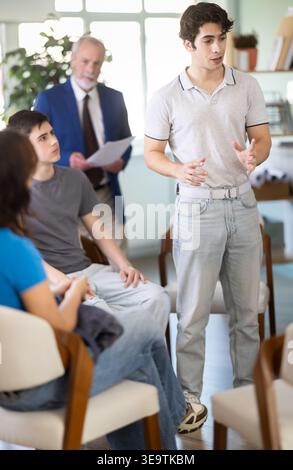 Young guy standing and talking to students sitting in a circle Stock Photo