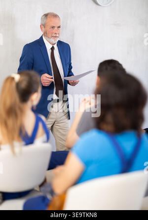 Senior teacher speaking to students in blue overalls Stock Photo