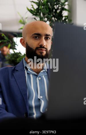 Arab businessman sitting in front of laptop at desk, preparing for video call with clients. Executive manager checking financial analytics report before presentation in coworking space Stock Photo
