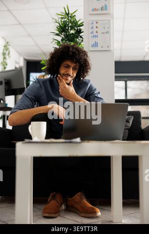 Arab company professional thinking about start up project development. Concentrated young entrepreneur solving complex strategy problem and working on laptop in business office Stock Photo