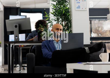 Smiling arabian businessman having videoconference with coworker in a corporate office. Project manager using a laptop for telework meeting in start up company coworking space Stock Photo