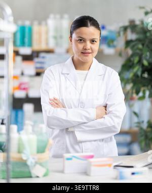 Confident female pharmacist standing behind counter with arms crossed Stock Photo