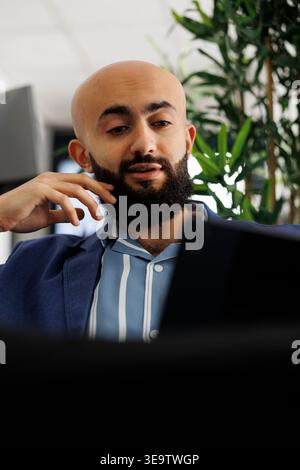 Arabian businessman having video call with coworker about startup project using digital tablet in coworking space. Executive discussing product launch with client in online meeting Stock Photo