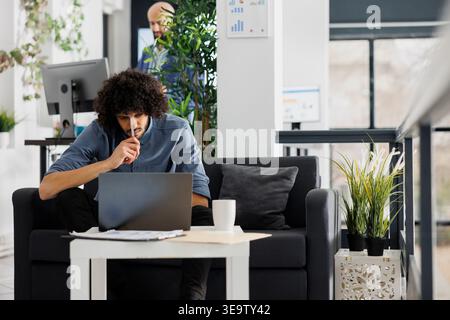 Tired employee watching tutorial video on laptop and taking notes to solve work task. Concentrated young arab executive manager analyzing product sales statistics on computer Stock Photo