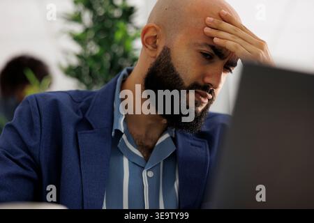 Arabian entrepreneur with migraine managing start up project at coworking space. Executive manager suffering from headache while working on marketing strategy in business office Stock Photo