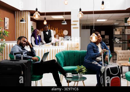 Tired people with luggage wait at hotel lobby, African American man and woman tourists wait to check-in. Black family couple arrived at resort for vacation, resting after long flight Stock Photo