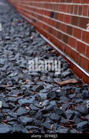 Close-up of dark gray landscaping rocks alongside a red brick wall with shallow depth of field and leading lines Stock Photo