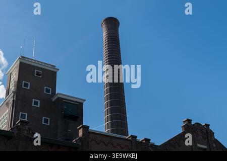 Tall brick industrial chimney stack rising above factory tower building against clear blue sky in Leiden, Netherlands. Low angle architectural view. Stock Photo