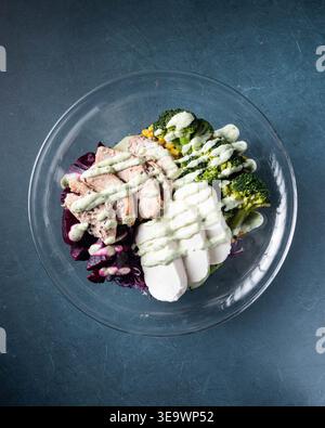 Fresh meal in clear bowl on dark textured surface. Salmon, broccoli, and sliced root vegetables with creamy drizzle. Simple, healthy, balanced dish. A Stock Photo