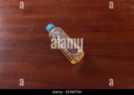 Small bottle containing liquid and white small bubbles. Shot on grainy textured brown wooden surface. Low-key lighting, focus on skincare, spa, or cle Stock Photo