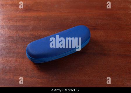 Studio shot. Blue glasses case with zipper closure on dark wooden surface. Soft, diffused lighting highlights textures. Useful for mockups, presentati Stock Photo