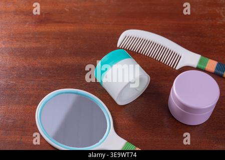 Still life showcases plastic containers,comb, hand mirror on dark wood. Features soft, diffused light, promoting wellness, cleanliness and beauty in a Stock Photo