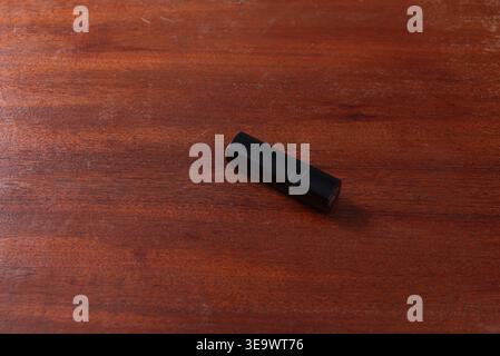 Studio shot featuring black lipstick tube isolated on a grained wood surface. Soft diffused lighting accentuates packaging texture and natural wood gr Stock Photo