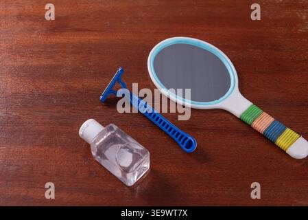Still life featuring a blue disposable razor, transparent sanitizer bottle, and round mirror with colorful handle. Studio shot, soft diffused lighting Stock Photo