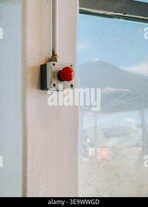 Valmiera, Latvia - April 18, 2026:Close-up of a red emergency stop button mounted on an industrial wall near a window. Highlights workplace safety, ha Stock Photo