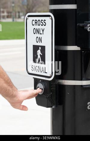 Vertical photo of a hand pressing the pedestrian crossing button at a U.S. crosswalk, activating the signal for safe pedestrian passage Stock Photo