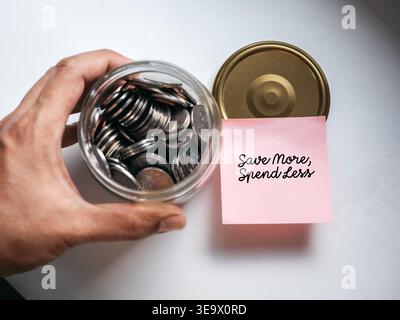 Saving money concept with post it note saying save more spend less and coins in jar. Budget planning, personal finance, financial goals. Stock Photo