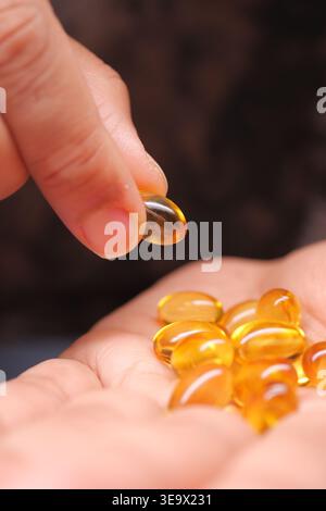 Holding a fish oil capsule in hand with others in palm Stock Photo
