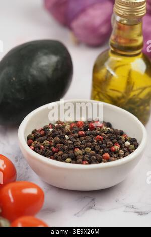 Mixed Peppercorns in a White Bowl with Cherry Tomatoes and Olive Oil on Marble Surface Stock Photo