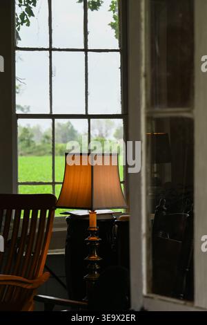 Small cottage door slightly open making a rocking chair and table lamp visible from the back light of a big window Stock Photo