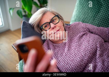 Senior woman lying on sofa and scrolling on phone. Stock Photo