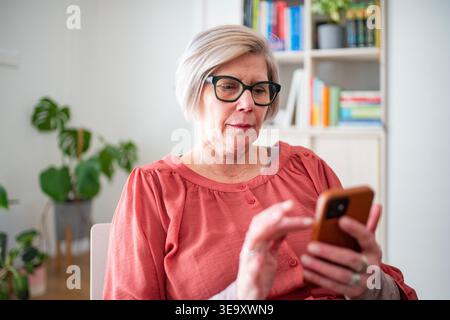 Older woman scrolling on phone while working from home during retirement. Stock Photo