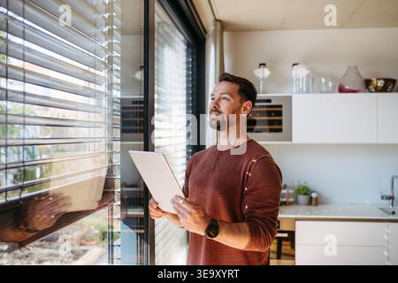 Man using smart home app to control electric window shades indoors. Stock Photo